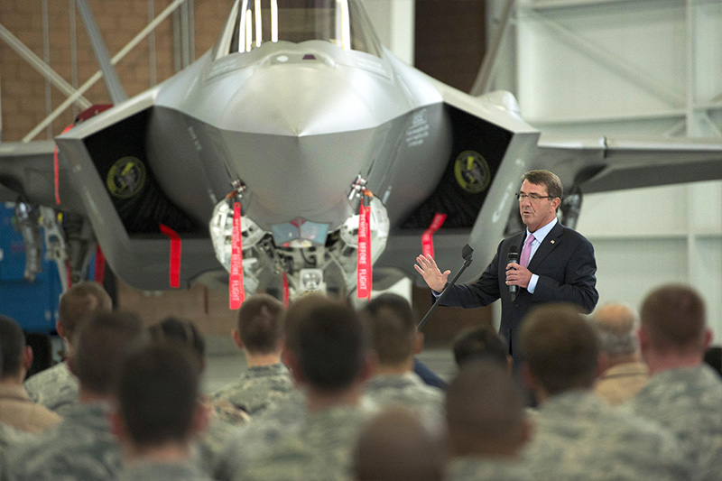 Defense Secretary Ash Carter speaking with service members with a jet in the background.