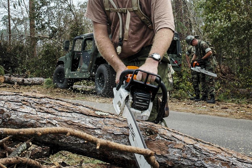 A Navy Seabee uses a chainsaw to remove fallen trees