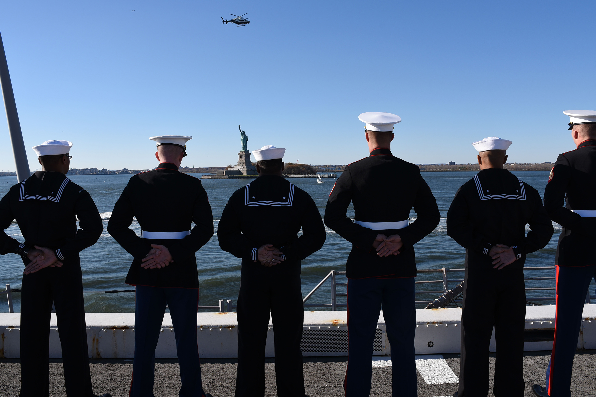Sailors and Marines stand at parade rest while manning the rails.