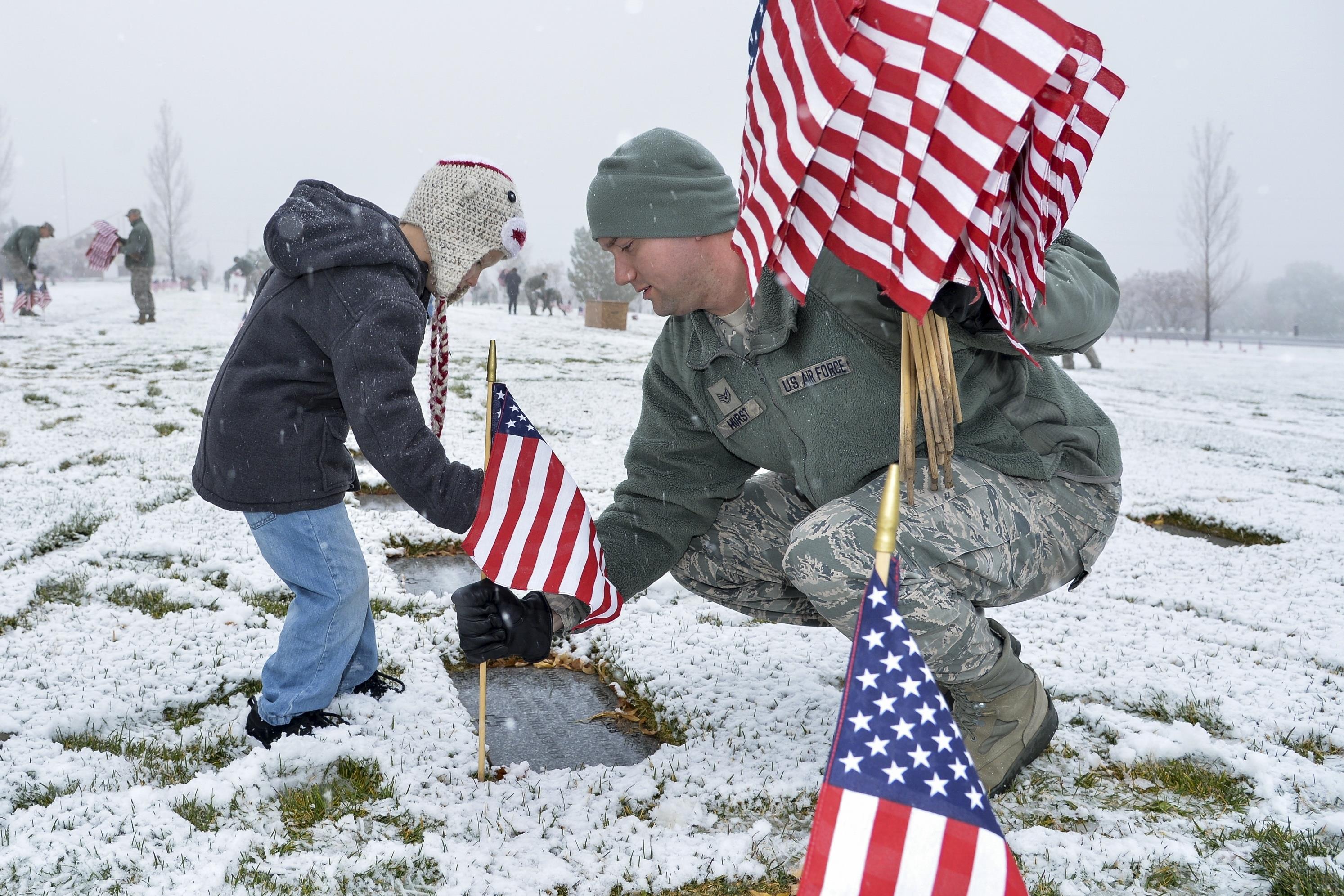 Air Force Staff Sgt. Louis Hurst and son, Ethan, place a flag beside a burial site