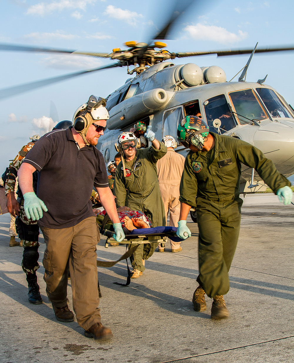 Relief personell carrying some affected by a disaster on a stretcher with a helicopter taking off behind them.