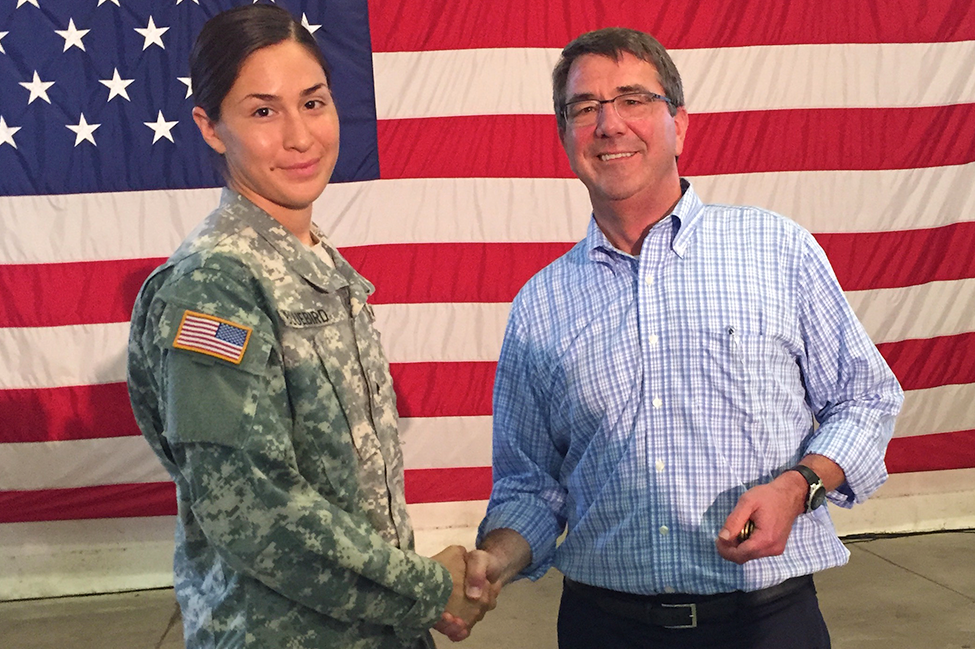 Defense Secretary Ash Carter shaking hands with Army Sgt. Terri Bluebird in front of an American flag
