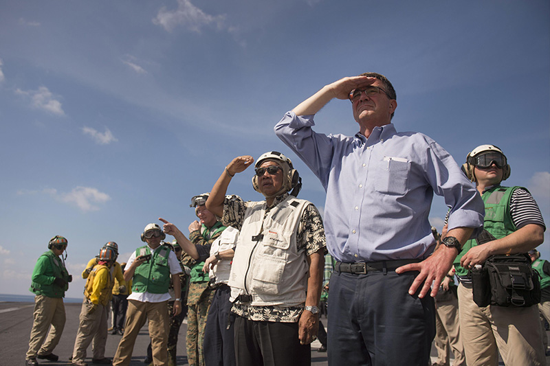 Defense Secretary Ash Carter and Philippine Defense Secretary Voltaire Gazmin standing on a flight deck shielding the sun from their eyes.