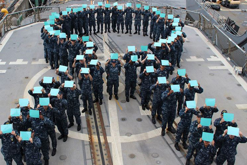 Sailors aboard the guided-missile cruiser USS Chancellorsville form a teal ribbon 