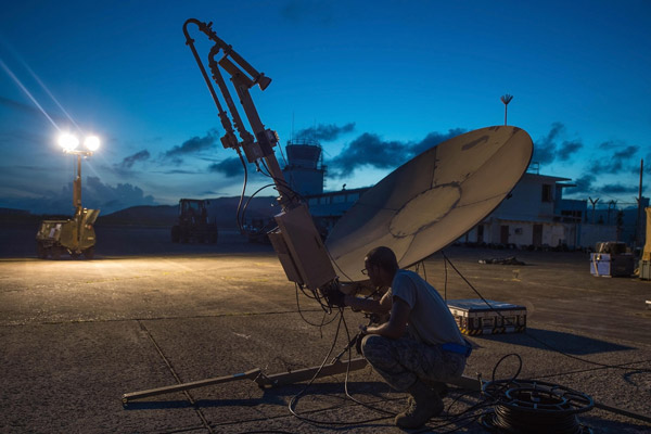 An airmen kneels next to a satellite communication antenna. 