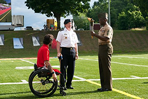 Dempsey standing next between an athlete in a wheelchair and a uniformed man hodling a torch. 2015 Warrior Games Closing Ceremony