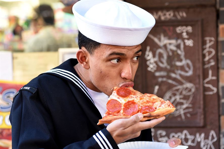 Navy Seaman Kevin Carranza takes a bite from a slice of pepperoni pizza