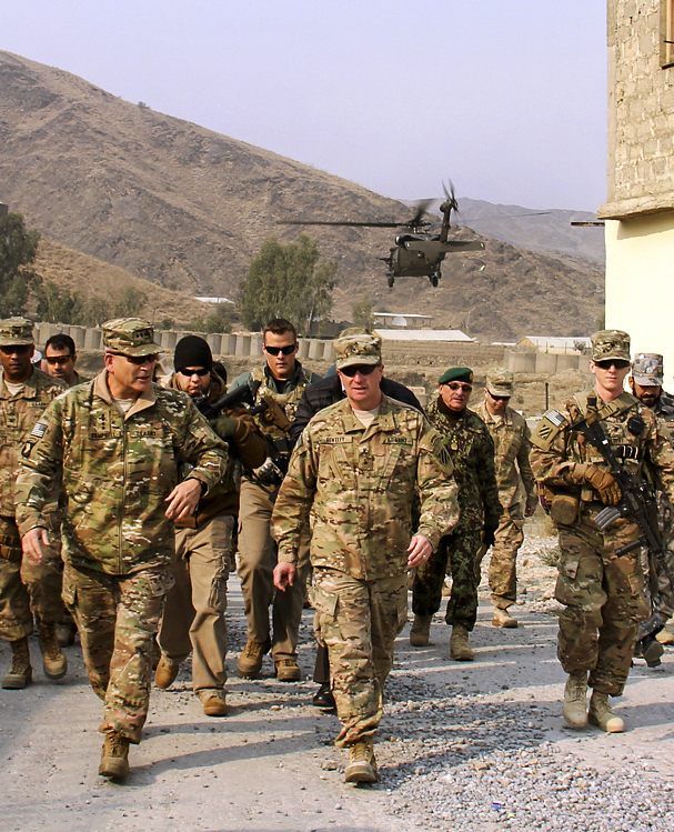 Troops walking with a helicopter in the sky behind them.
