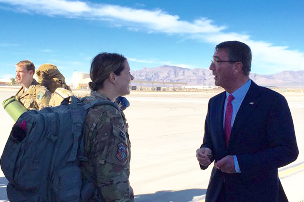 Defense Secretary Ash Carter speaking with a female servicewoman wearing camouflage and a large backpack with mountains in the background 