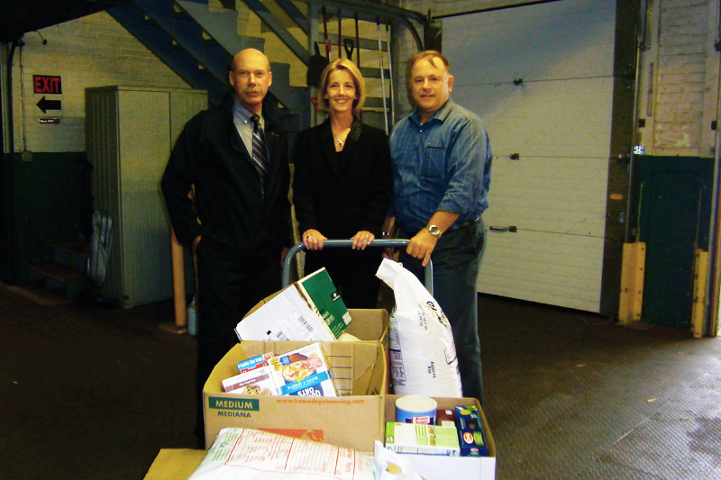 This image shows Tim Hulub, Virginia Morrissette and Jim Herbert standing with boxes of donated food.