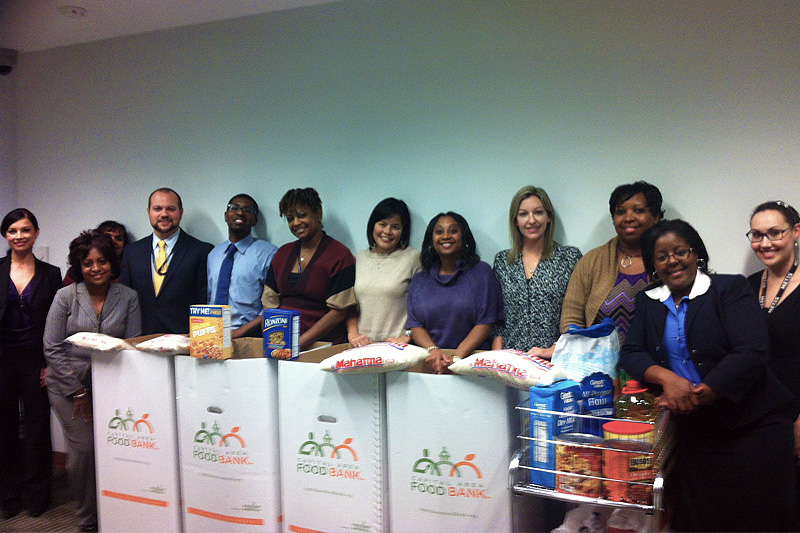 This image shows a line of Defense Security Service employees standing behind four Capital Area Food Bank donation boxes and nonperishable food items.