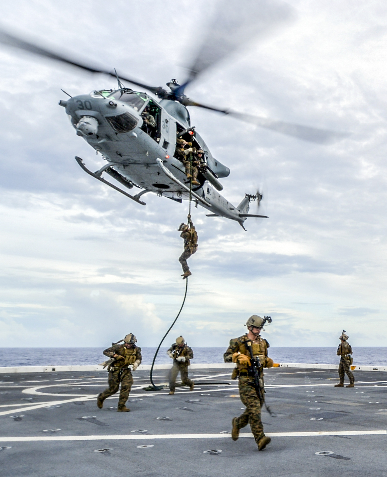 Navy Petty Officer 2nd Class Ramiro Alvarez directs a UH-1 Huey helicopter as Marines repel during fast-rope training aboard the USS Somerset in the Pacific Ocean.