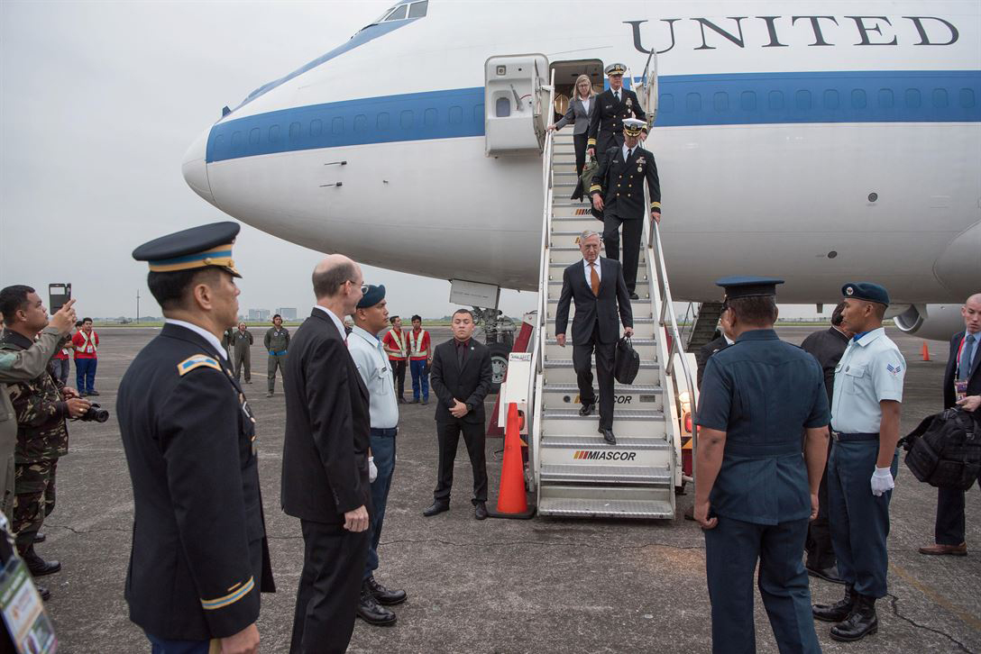 Defense Secretary Jim Mattis walks down stairs from an aircraft onto a flightline, where people wait to greet him.