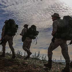 Three service members walk with backpacks.
